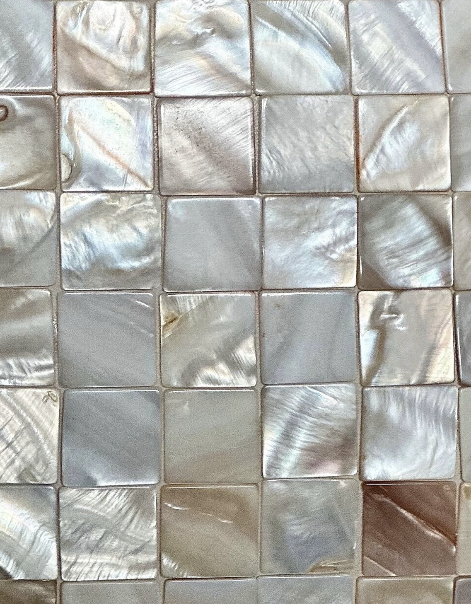 Close-up of a mosaic wall made of iridescent mother-of-pearl tiles arranged in a grid pattern.