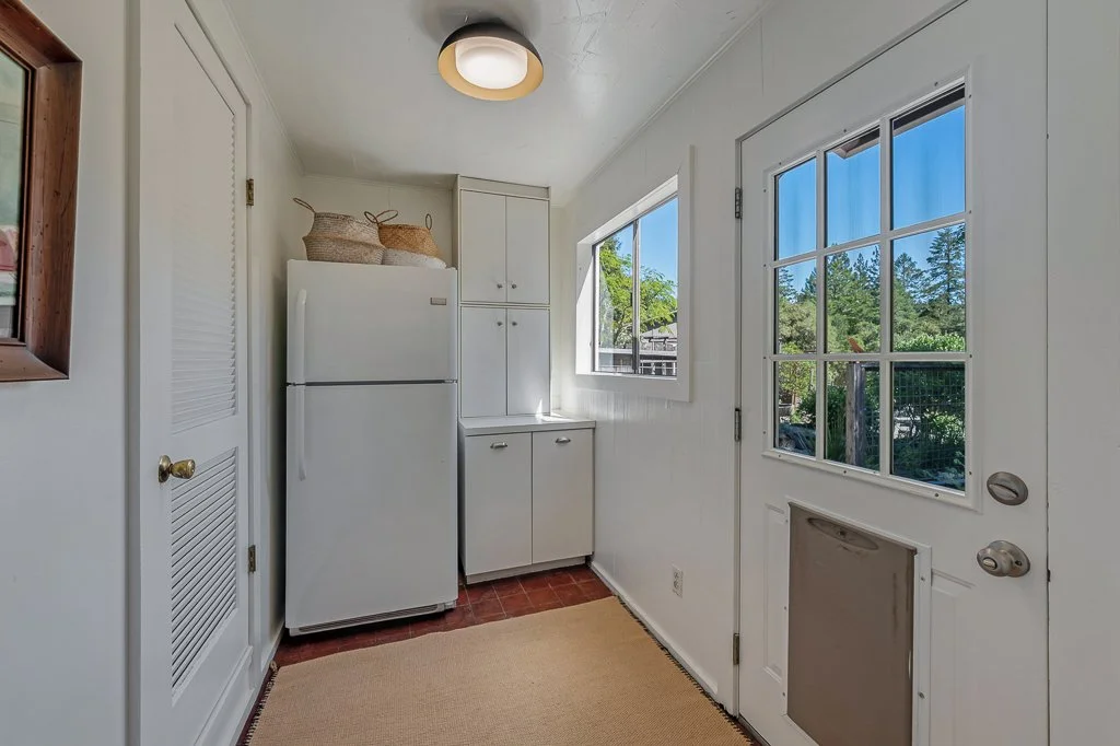 A cozy white kitchen entryway with a refrigerator, white cabinets, a window, and a door with glass panes leading outside.