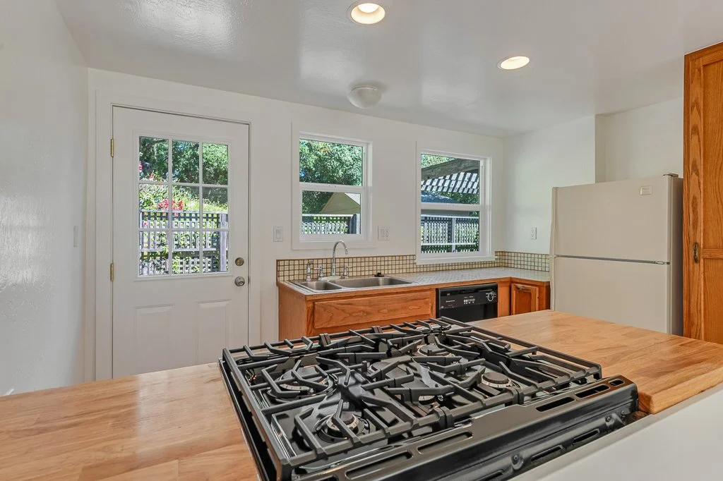 Kitchen with a gas stove, white refrigerator, wooden cabinets, and windows showing a garden outside.