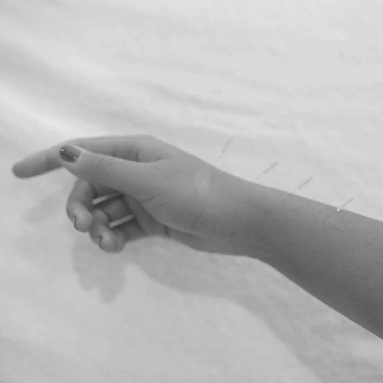 Close-up of a hand with a small tattoo on the ring finger, holding a white object with four visible prongs or pins, possibly a plug or connector, on a light background.