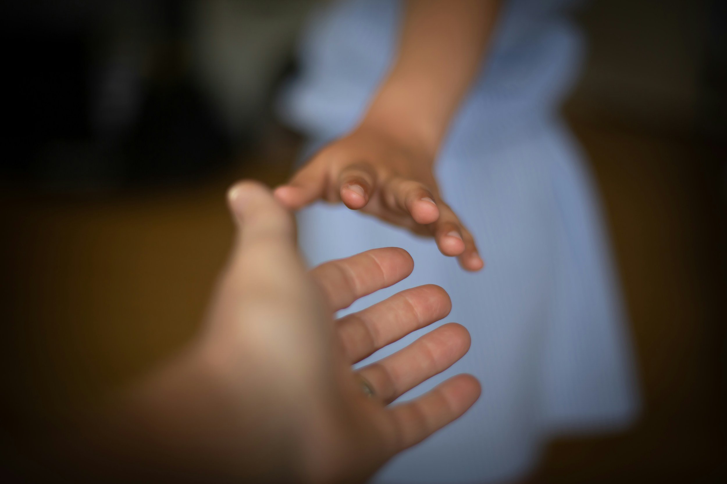 Close-up of two hands reaching out and holding each other, with a blurred background.