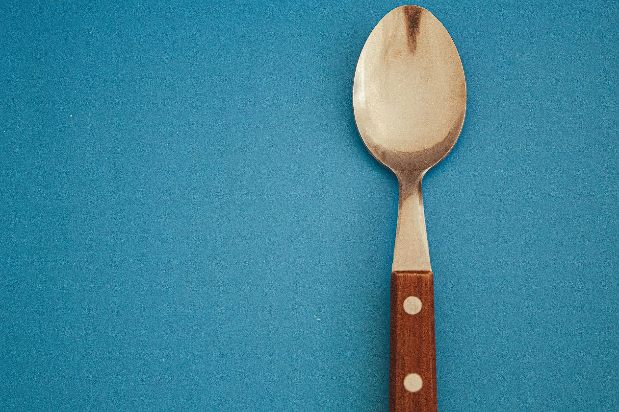 bronze metal spoon with wooden handle over a blue background.
