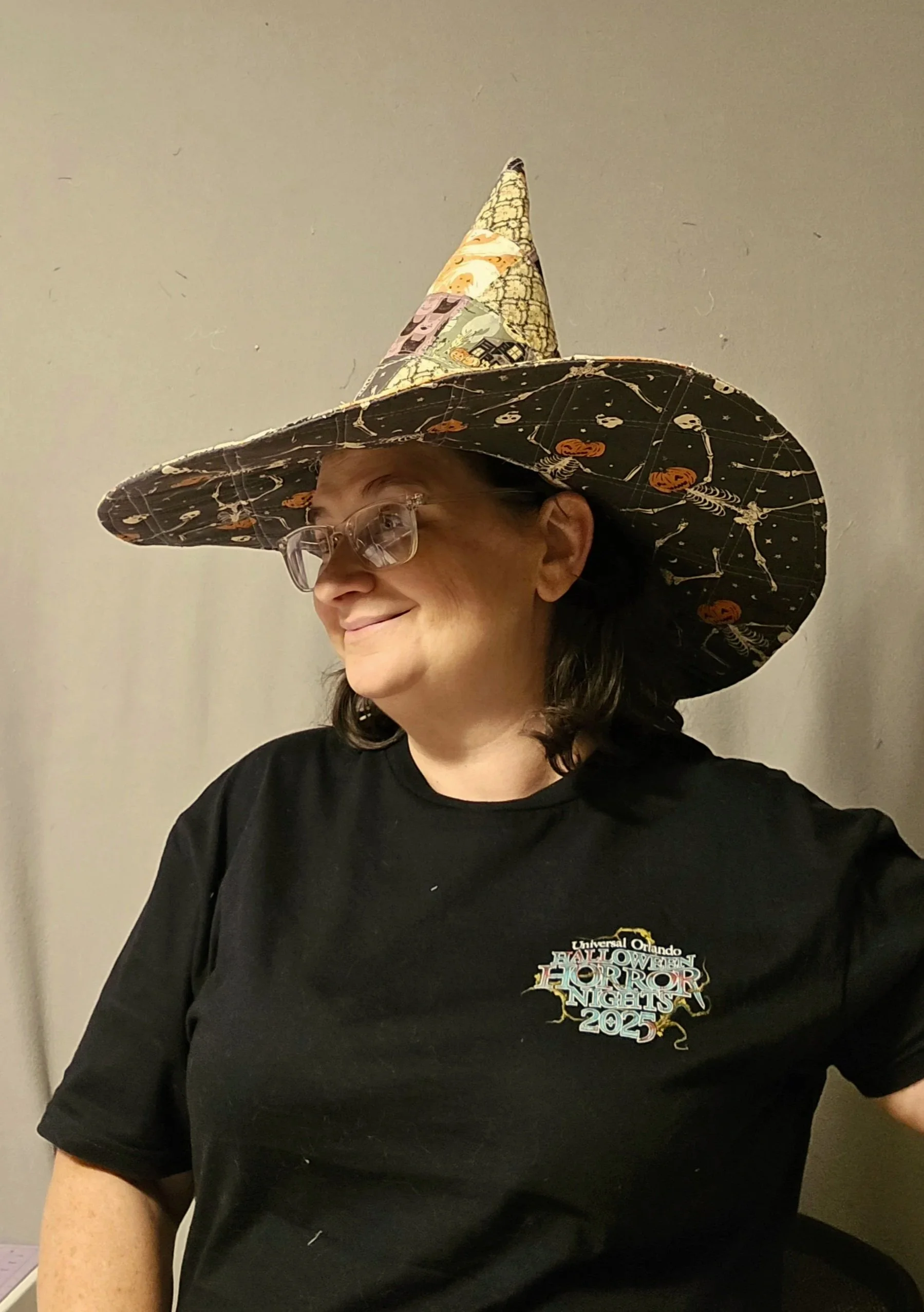 Woman wearing a Halloween themed witch hat and a black T-shirt with a horror nights 2025 logo.