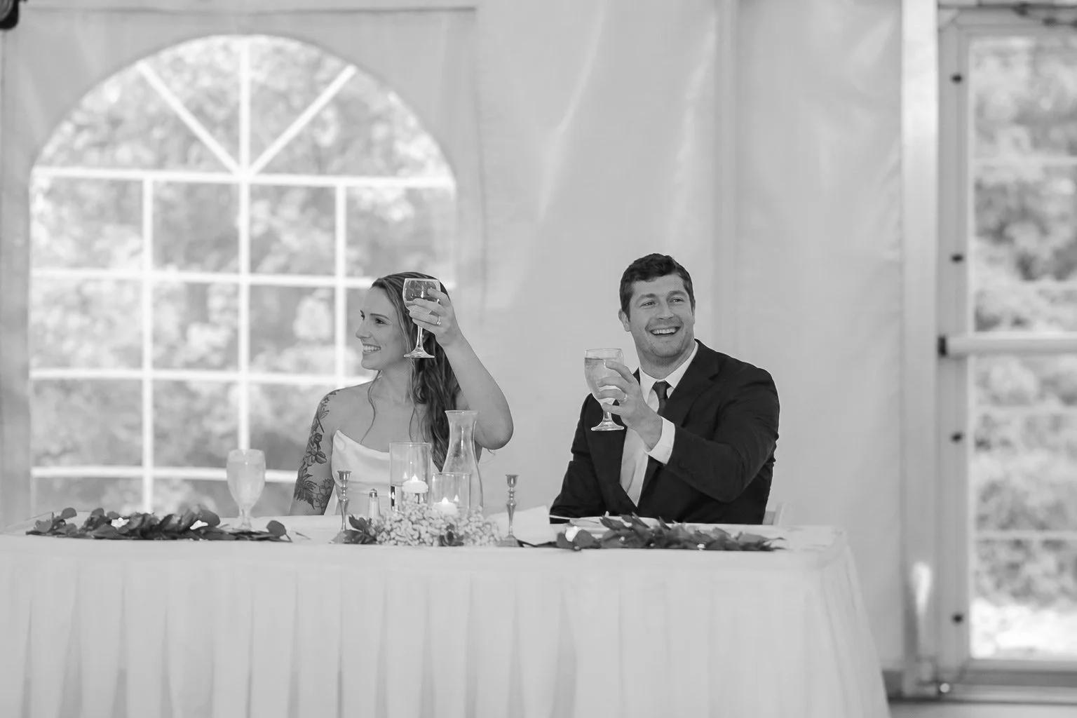 A smiling man and woman raising glasses at a wedding reception.
