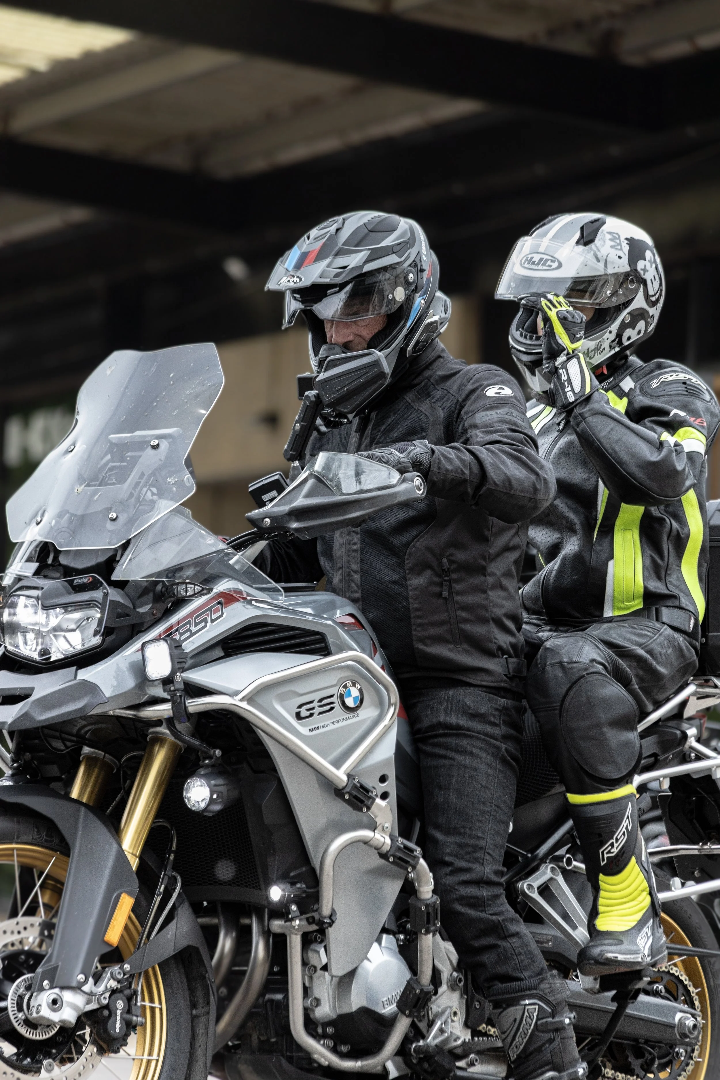 Two motorcyclists in full gear, including helmets, riding a BMW motorcycle on a city street.