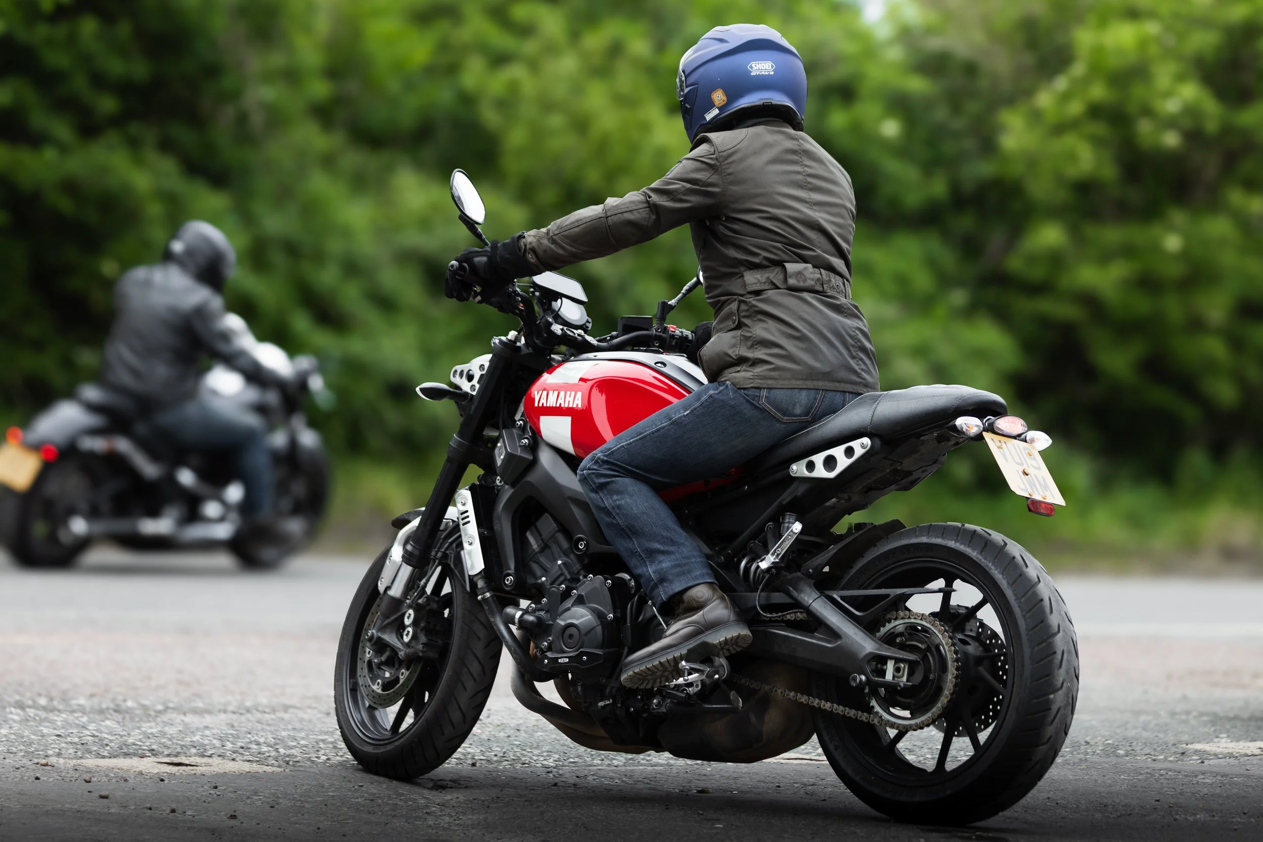 A person riding a red Yamaha motorcycle on a paved road with greenery in the background, wearing a blue helmet and gray jacket.