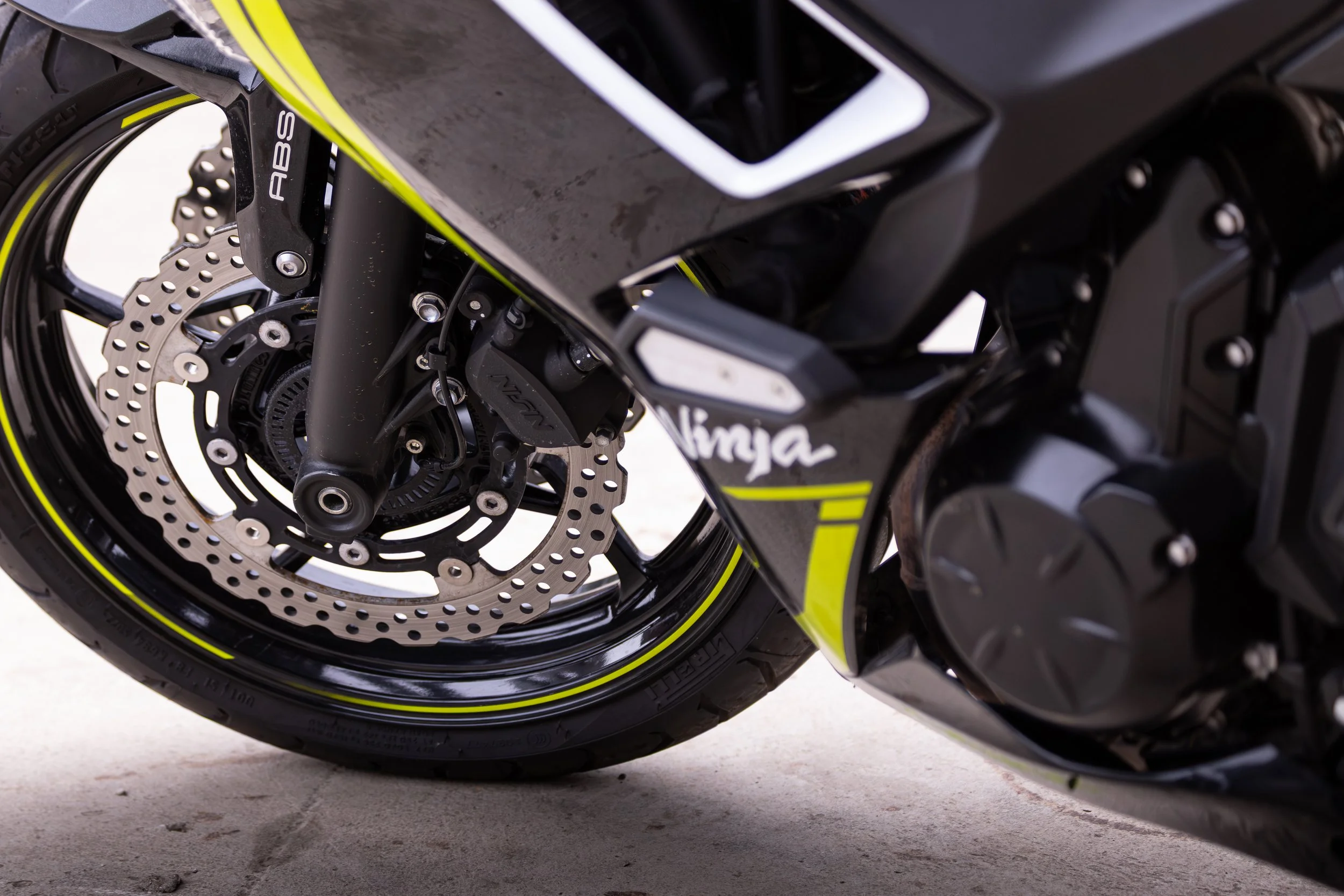 Close-up of a black and neon yellow motorcycle front wheel, featuring a disc brake, tire, and part of the fork.