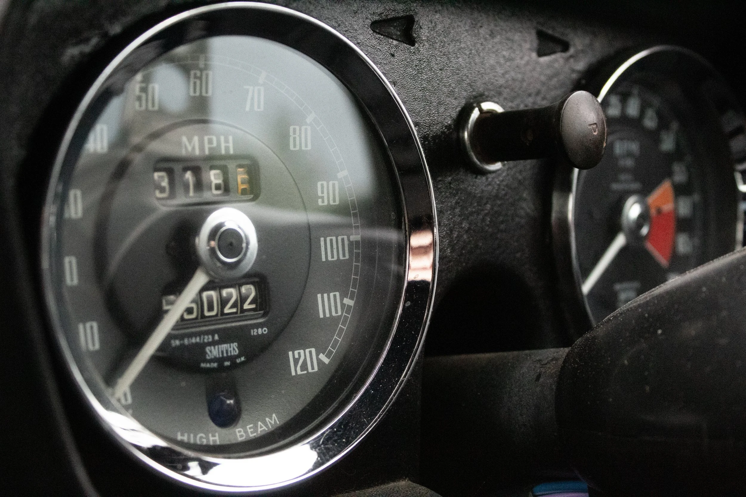 Close-up of a vintage car dashboard with a speedometer, odometer reading 318 miles, and a gauge showing high beam status.