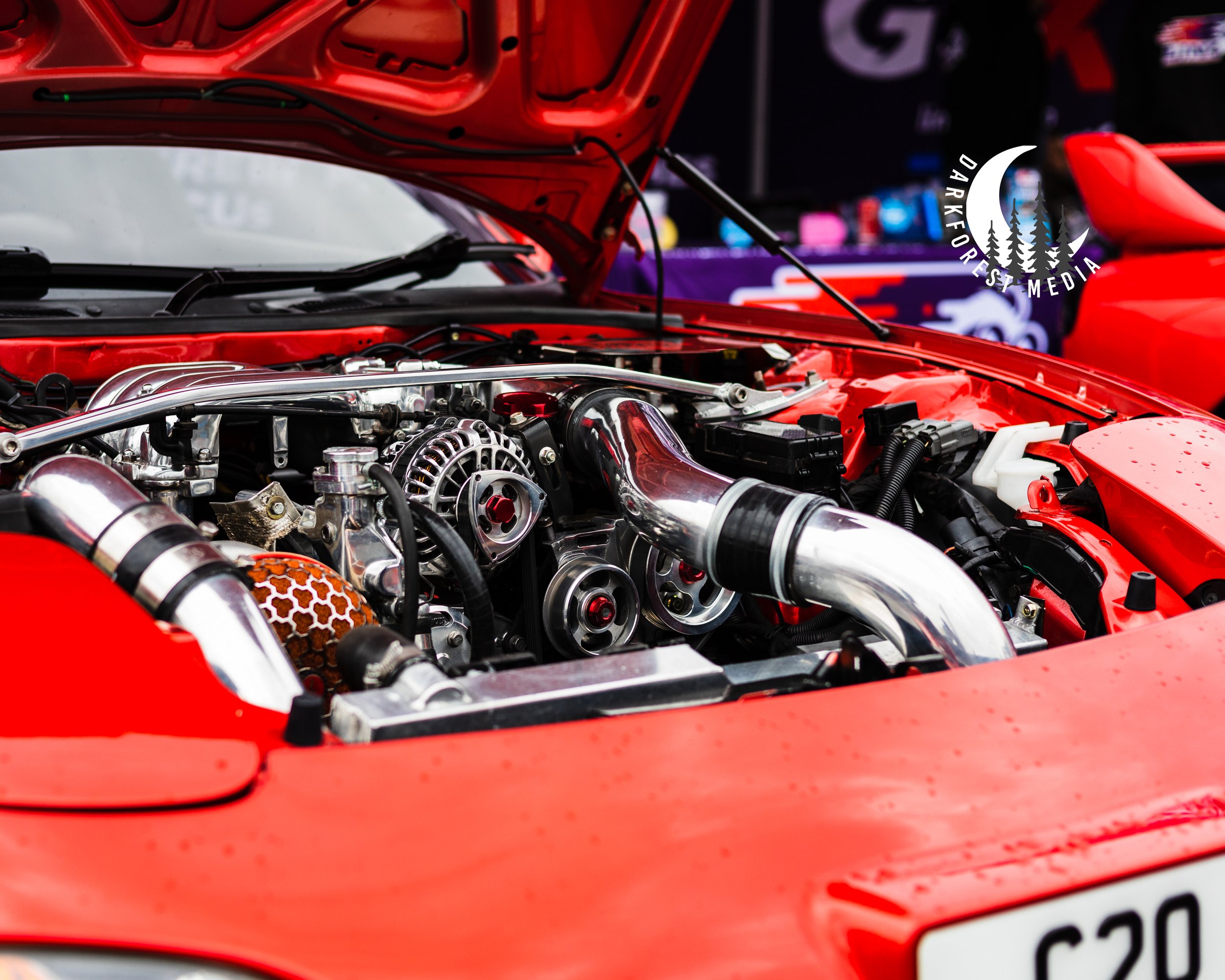Inside view of a red car engine with the hood open, showing various engine components and parts.