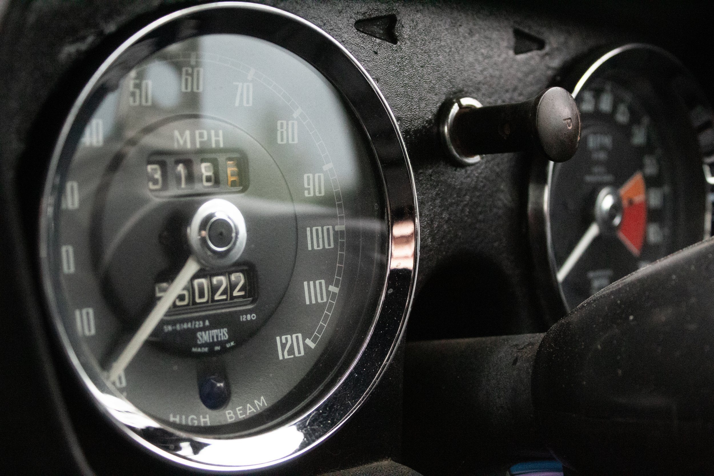 Close-up of a vintage car dashboard showing speedometer, odometer, and various gauges, with a focus on the speedometer needle pointing to 0 MPH.