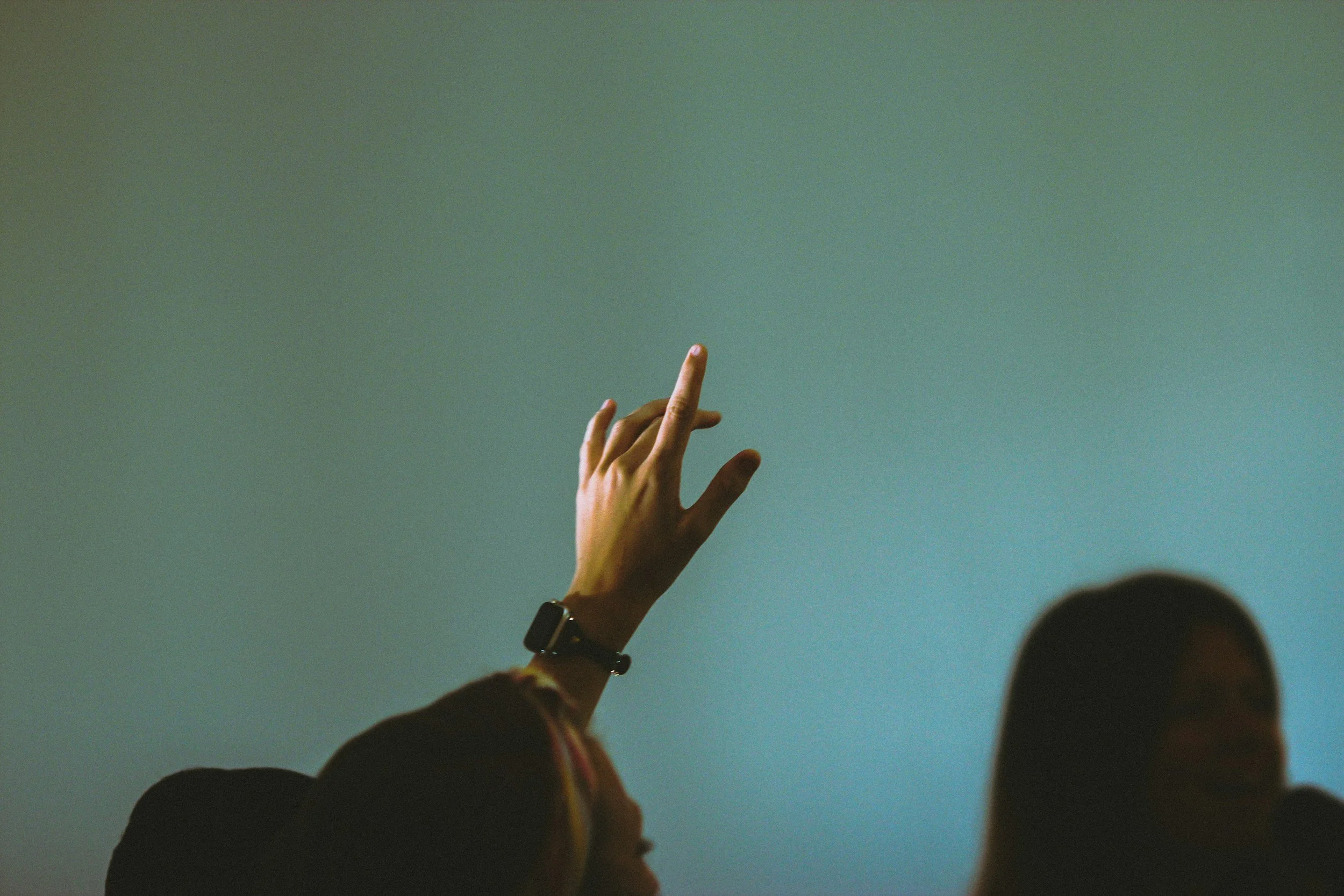 Person raising hand to ask question against a turquoise background.