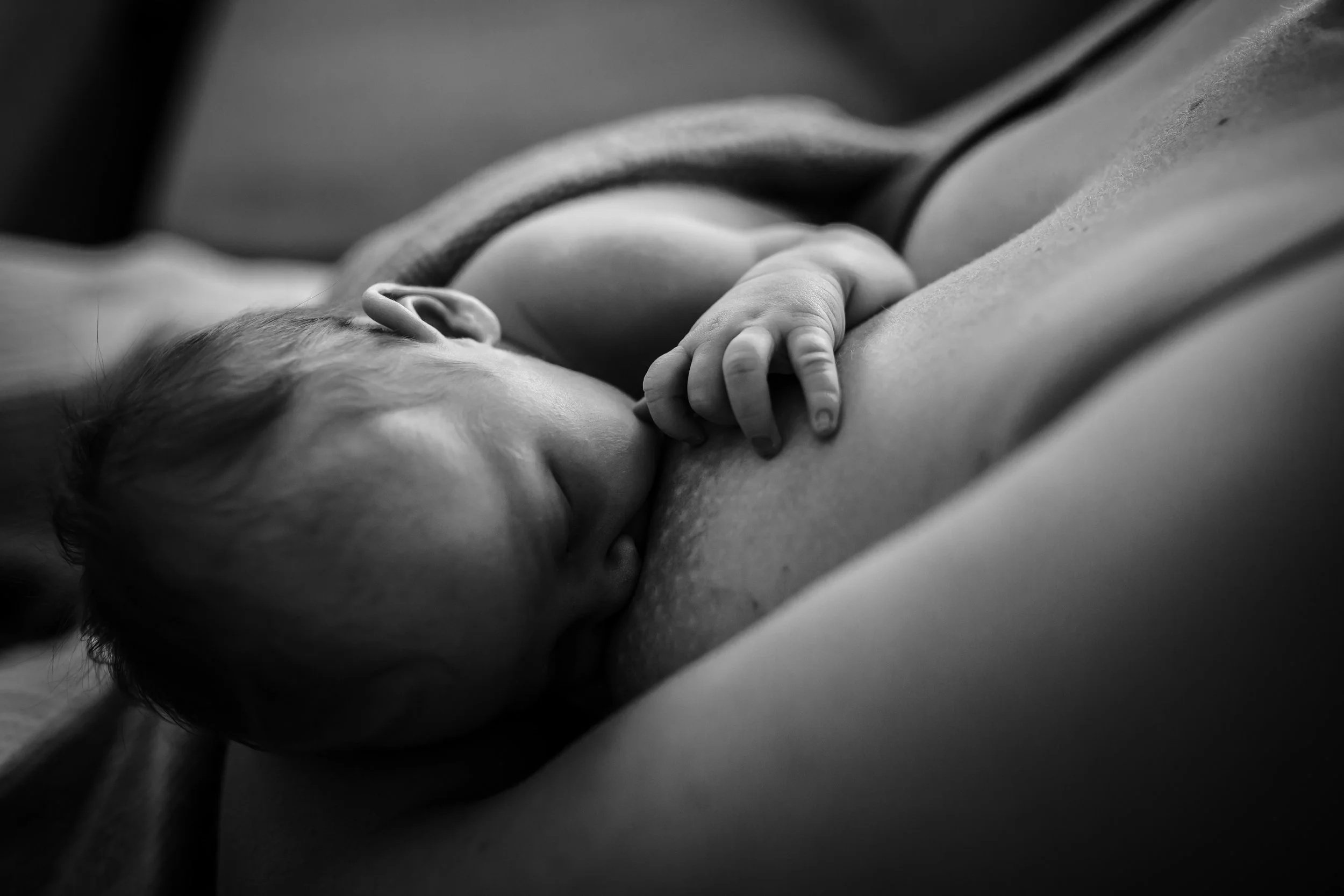 A black and white close-up of a sleeping baby lying on a soft surface, with a hand resting gently near their face.