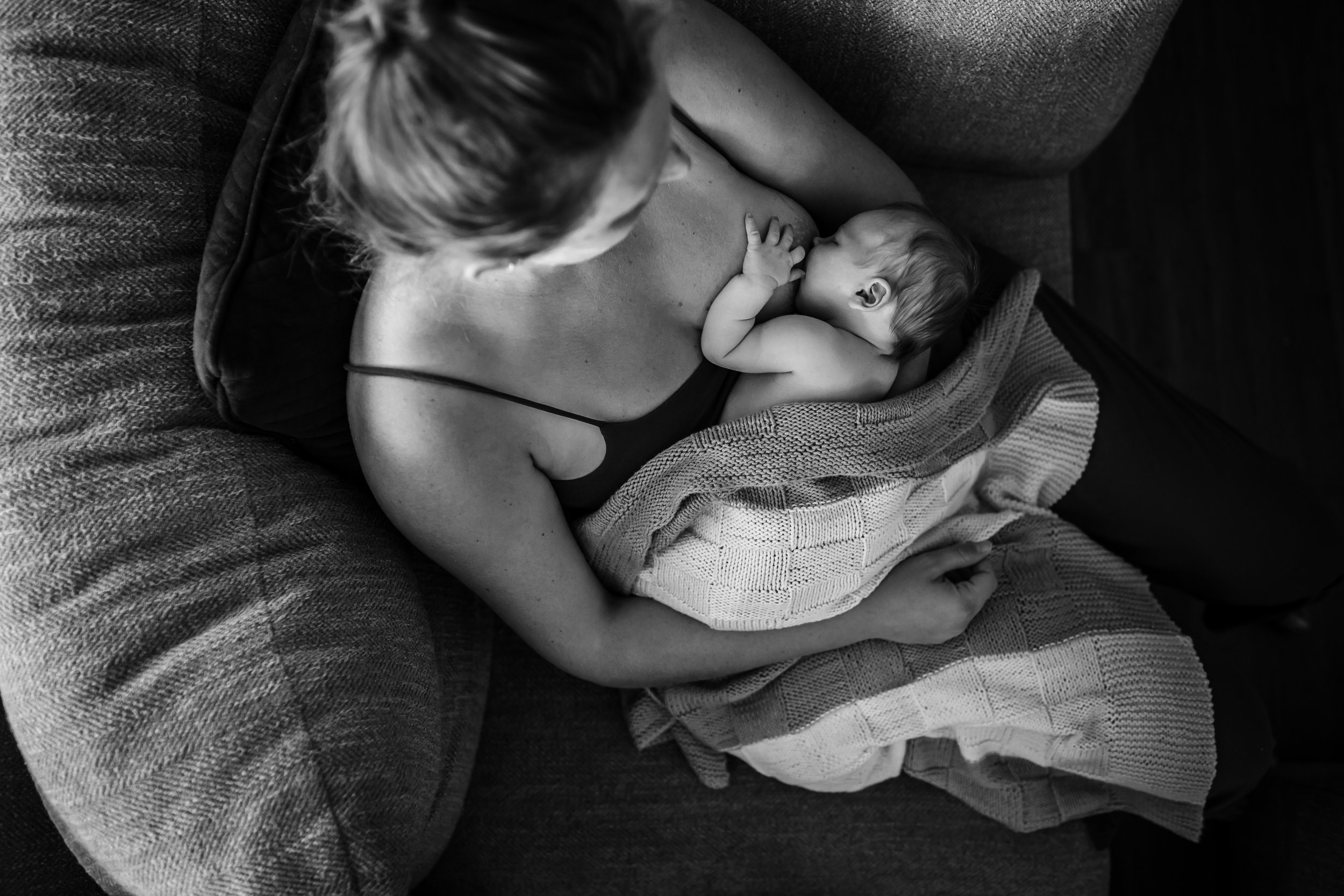 A woman breastfeeding a baby on a sofa, with a blanket draped over her lap, in black and white.