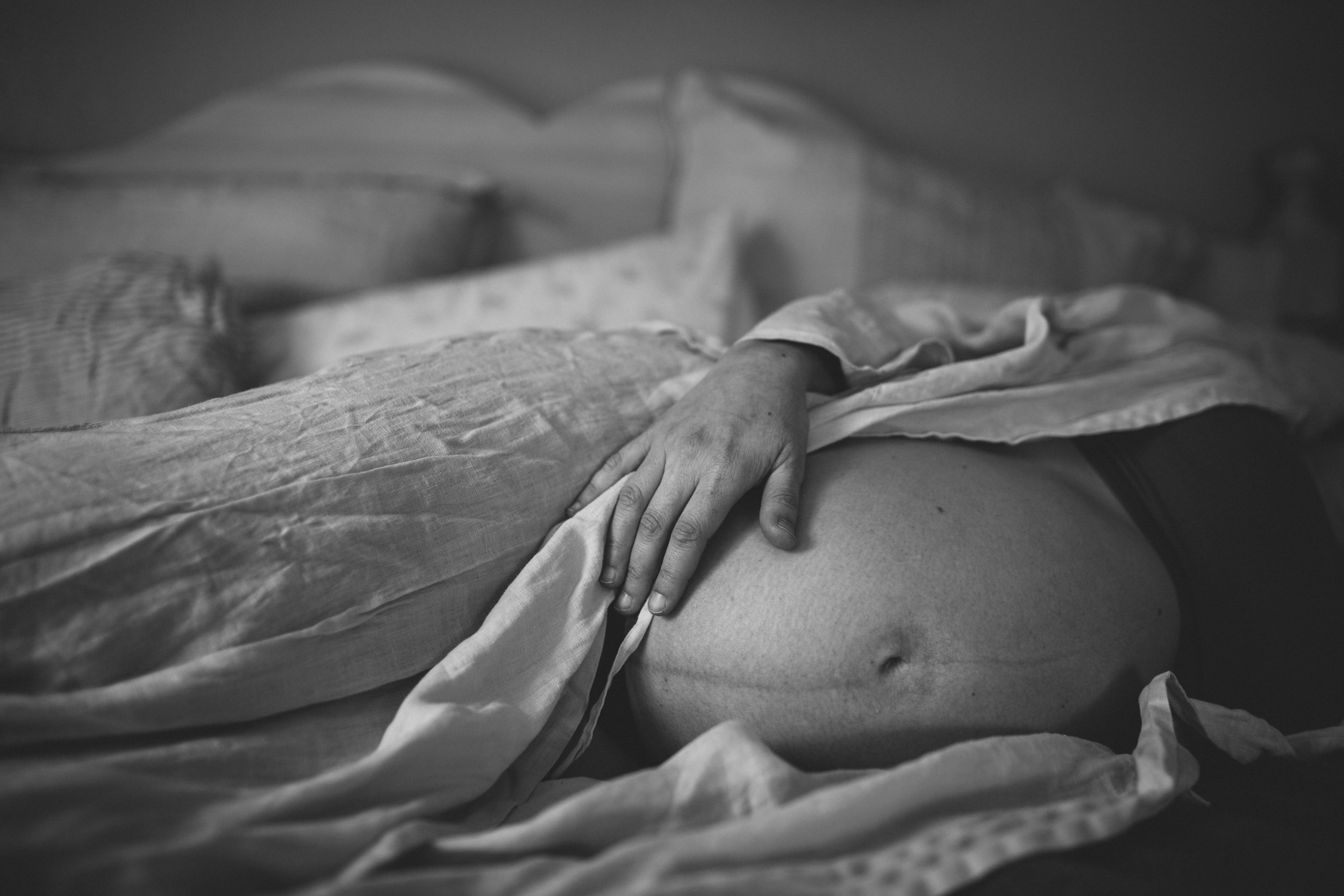 Close-up of a person's hand resting on a hospital bed covered with a sheet, indicating a hospital or medical setting.