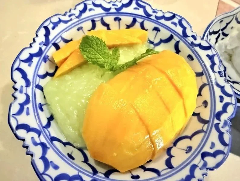 A bowl with sliced mango, green melon with mint leaves on top, and some sliced pieces of mango. There is also a side dish of white rice in a separate bowl.