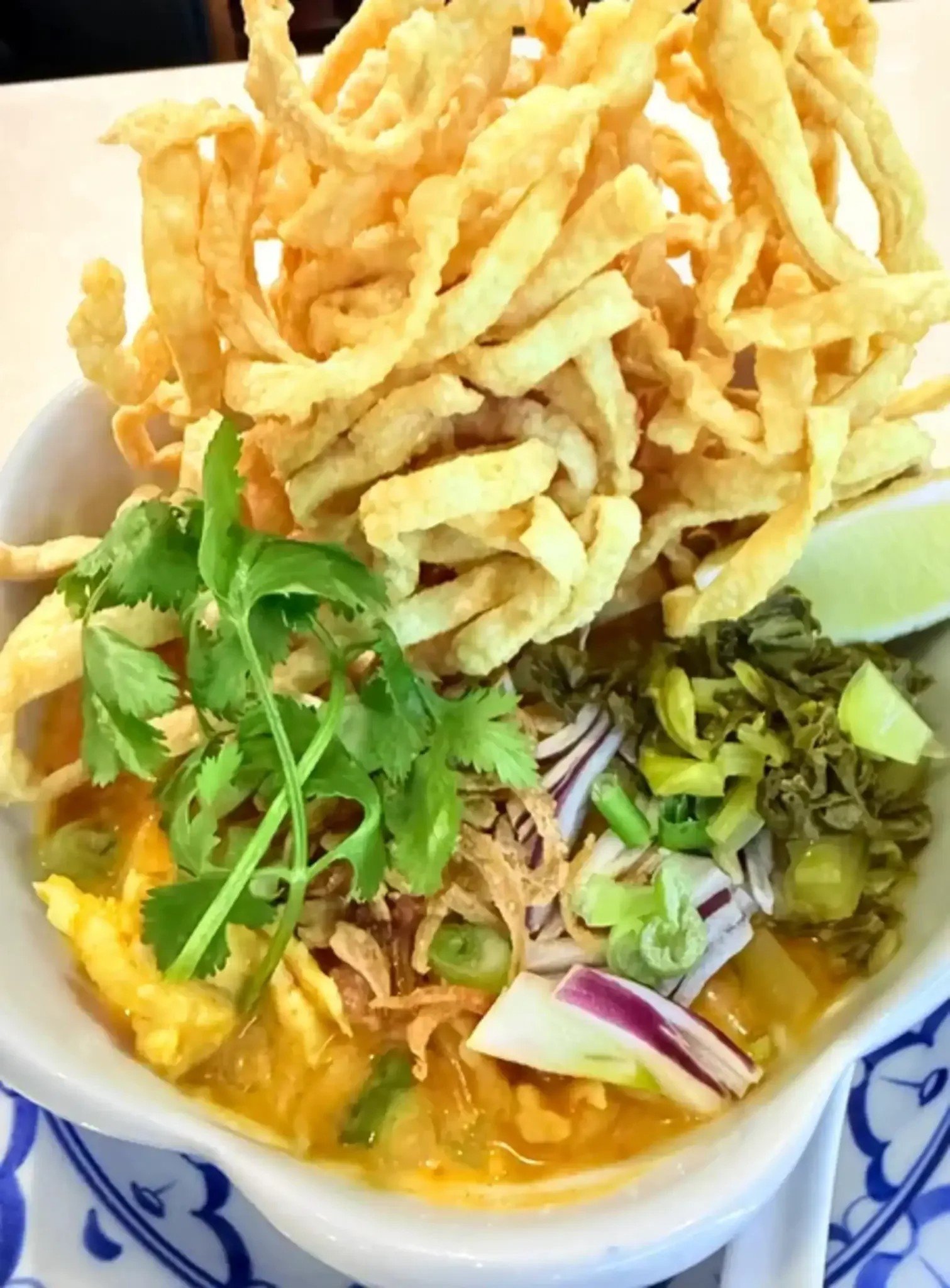 Bowl of Thai yellow curry with fried noodles, fresh cilantro, assorted vegetables, and slices of lime.