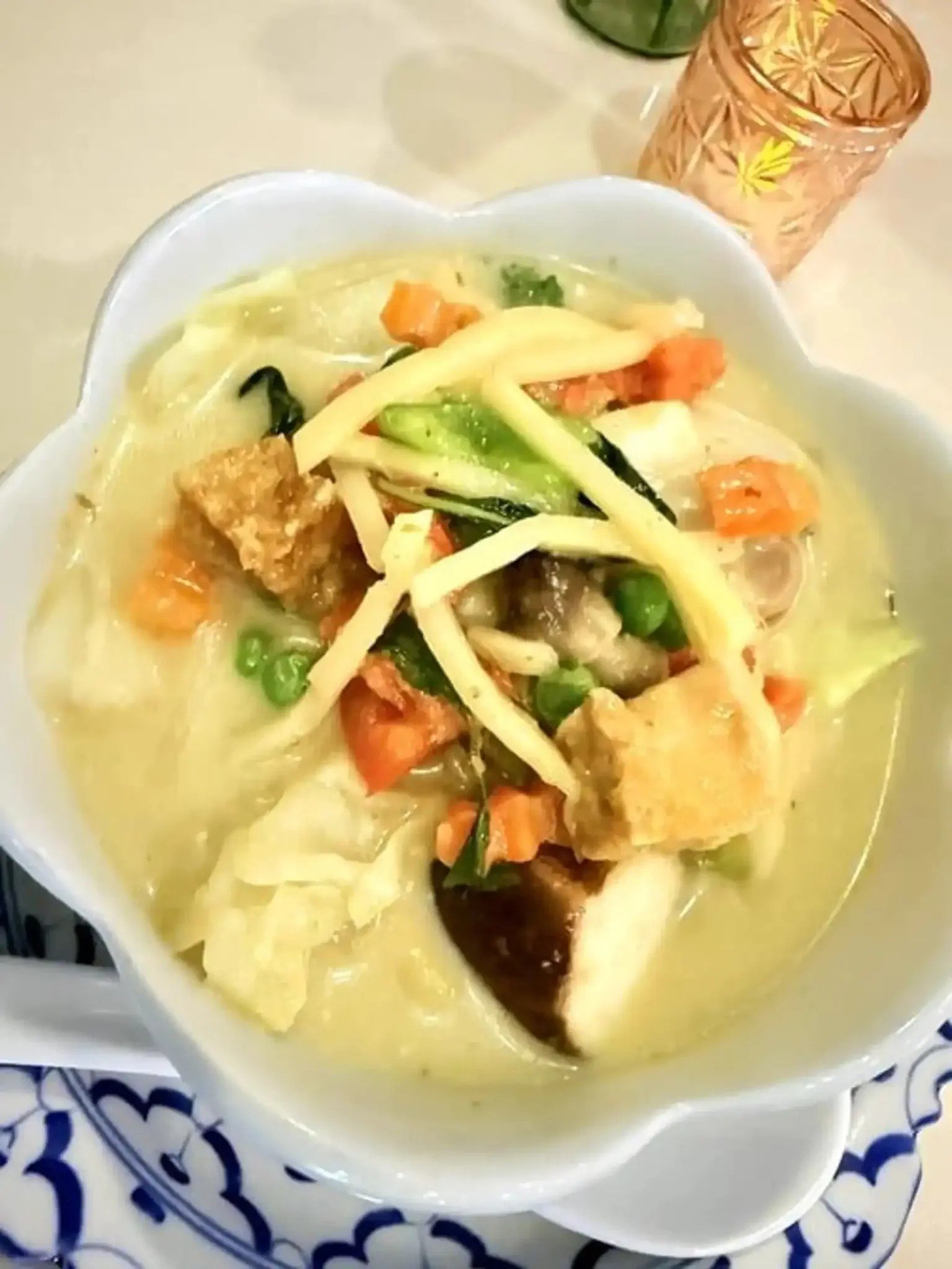 A bowl of chicken vegetable soup with carrots, green beans, and cabbage, garnished with herbs, served in a white bowl.