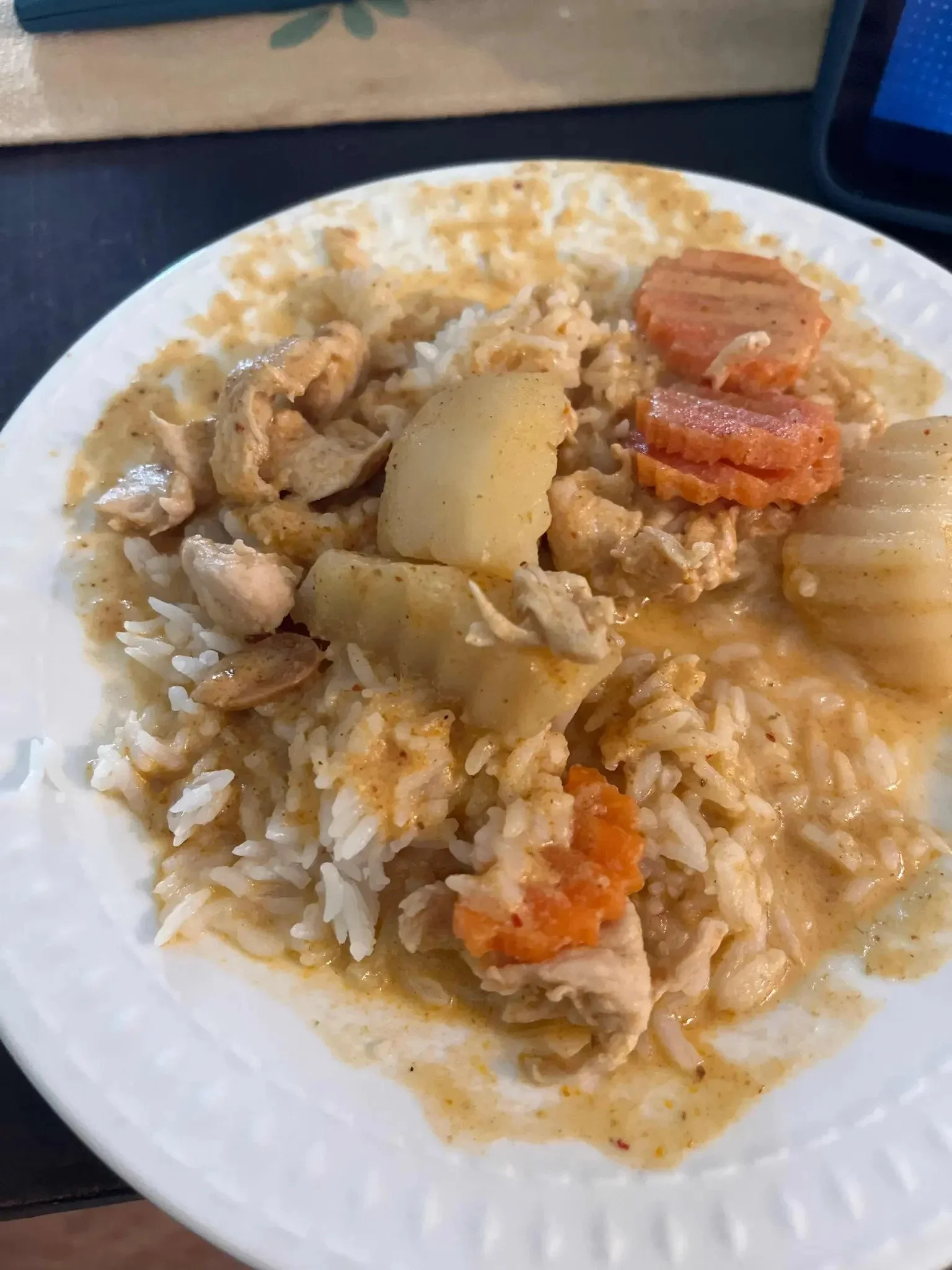 A white plate with rice, cooked chicken, potatoes, carrots, and onions in a creamy sauce.