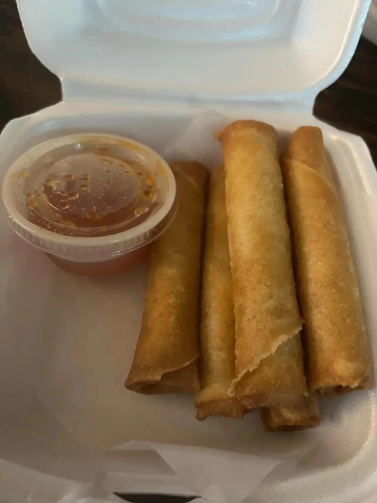Four fried egg rolls with a small container of dipping sauce.