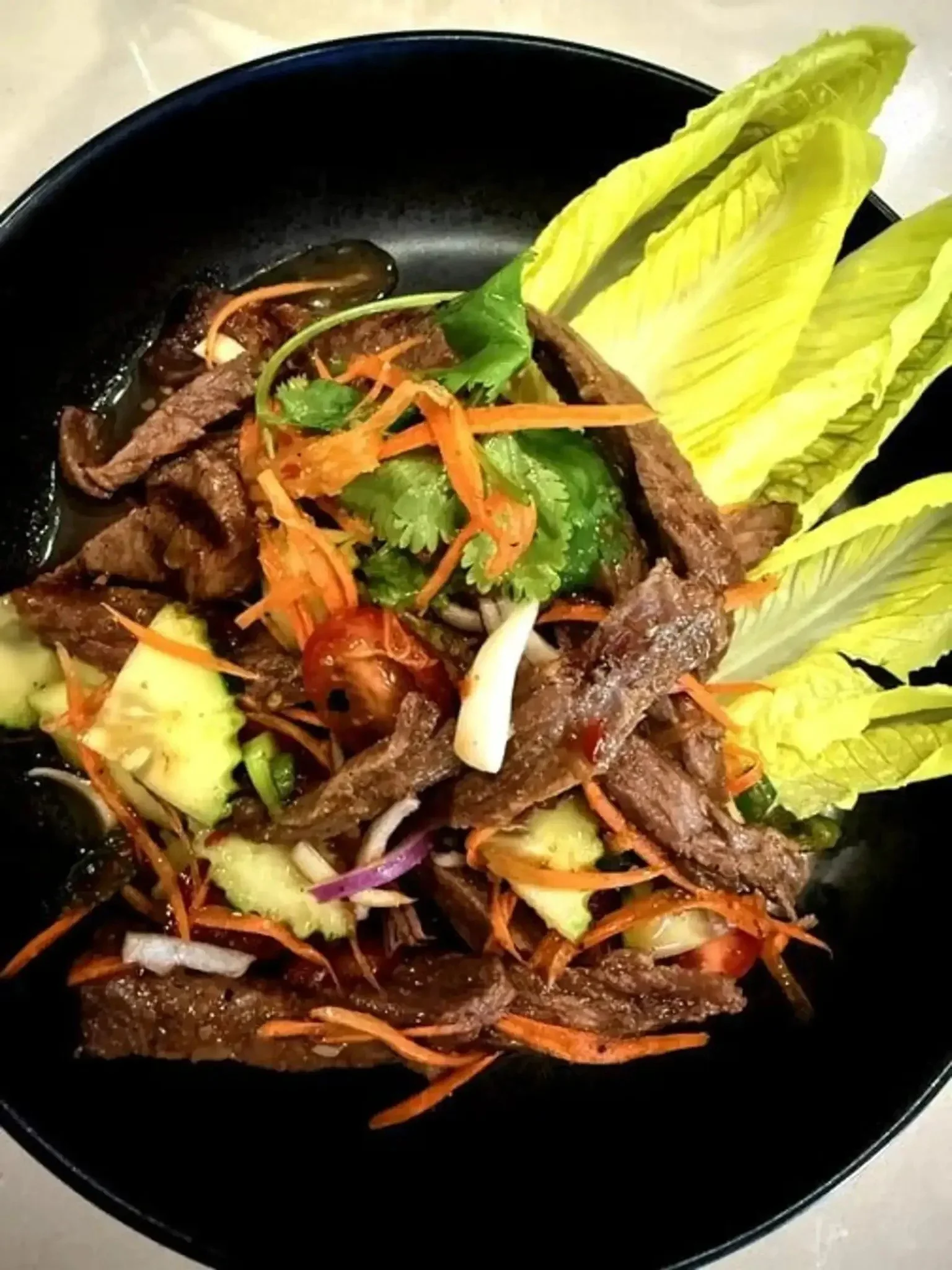 A bowl of Asian-style beef stir-fry with sliced beef, vegetables, and garnishes.