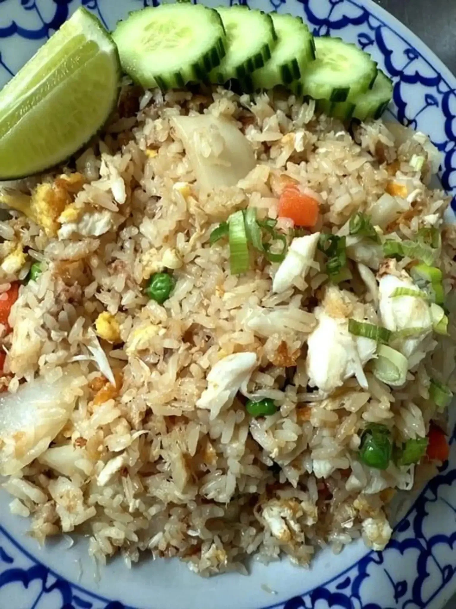 A plate of fried rice garnished with sliced cucumber and a lemon wedge.