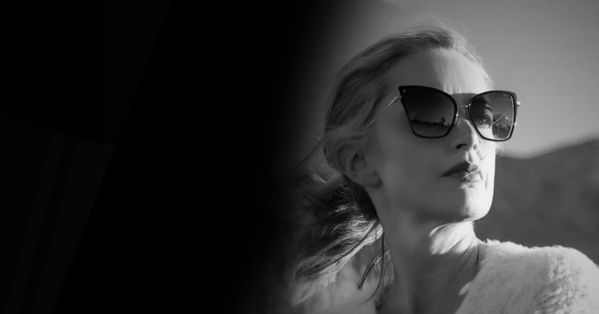 A black and white photo of Claire Von Cleveland wearing large sunglasses, with mountains in the background.