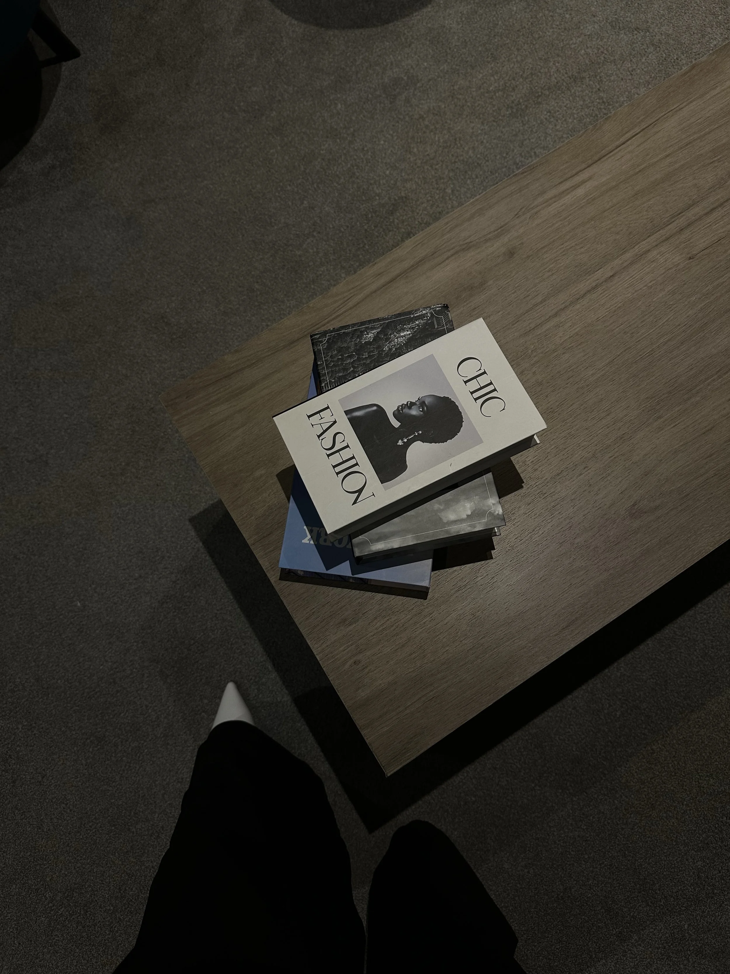 A wooden table with several magazines stacked on top. The top magazine features a black-and-white portrait of a woman and the words "Chic Fashion".