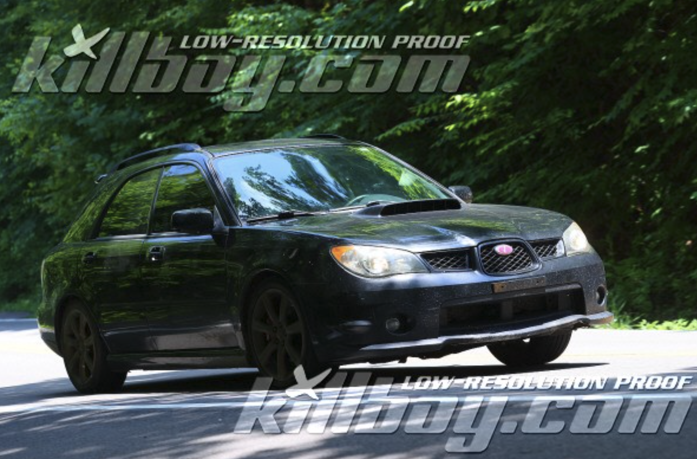 A black Subaru Outback driving on a road surrounded by green trees.