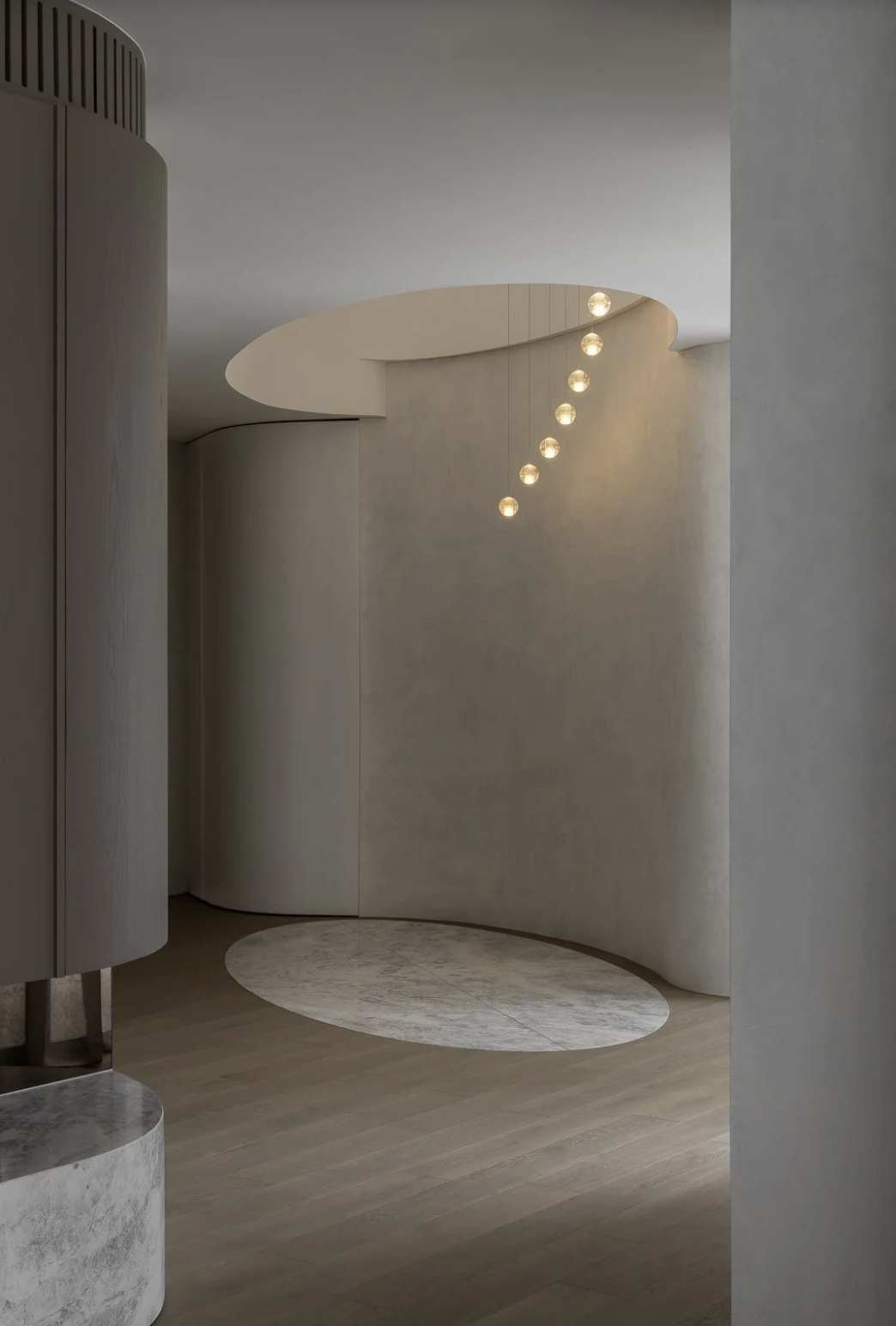 Minimalist interior with curved white walls, a set of hanging globe pendant lights, and a wooden floor with a circular rug.