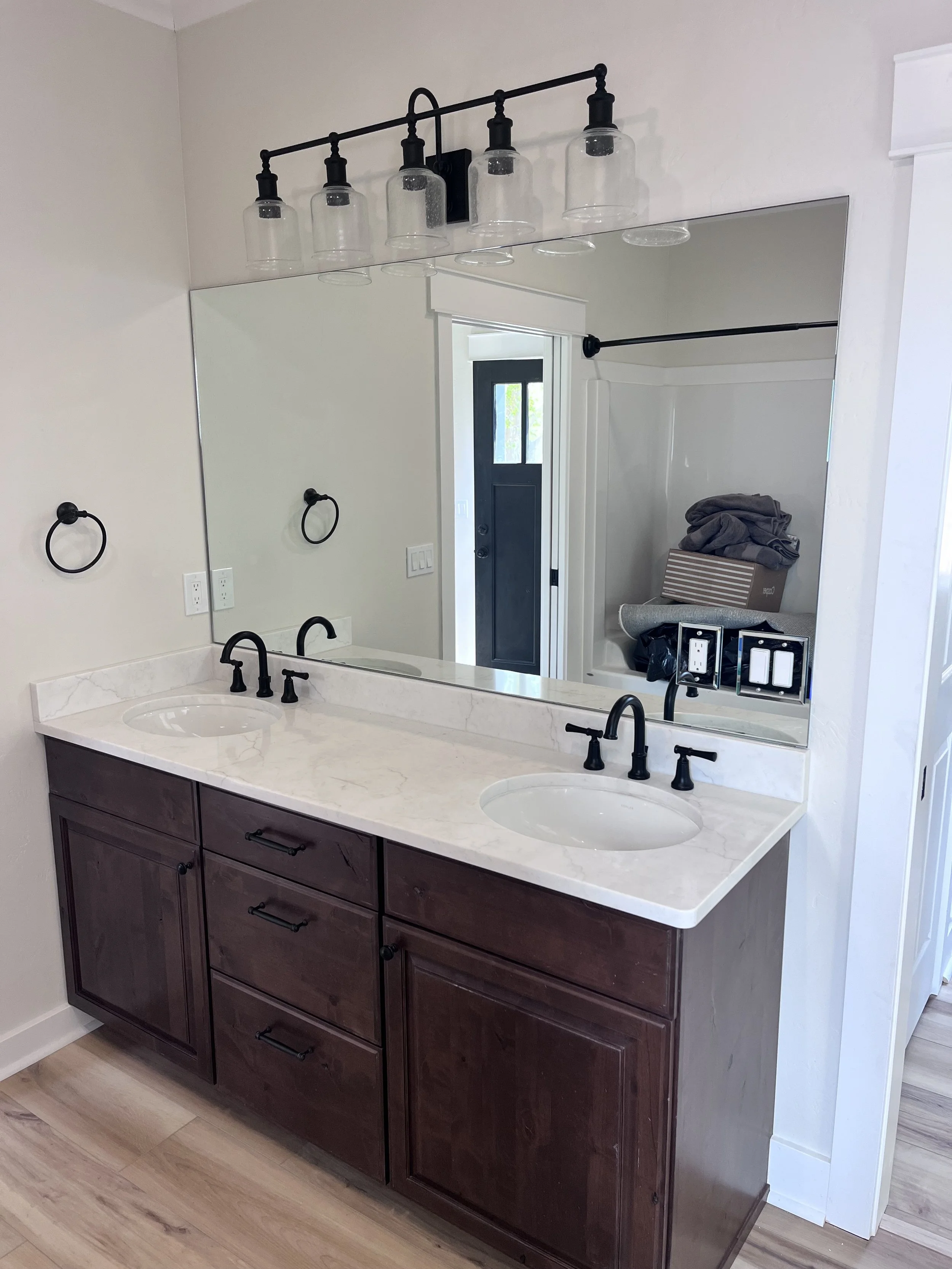 Bathroom vanity with two sinks, dark wood cabinet, marble countertop, large mirror, black faucet, and four black light fixtures with glass shades above the mirror.