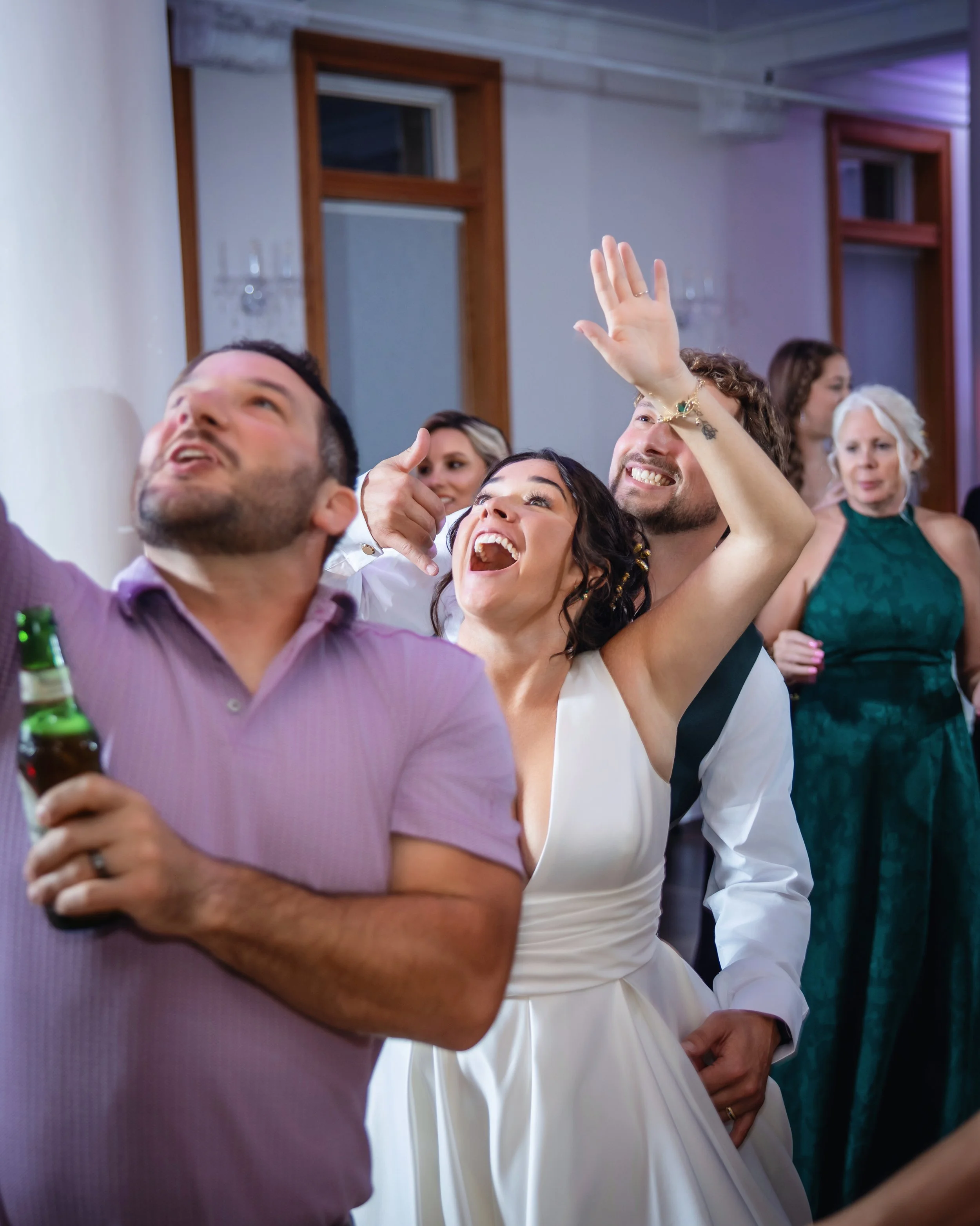 People at a social gathering, smiling and celebrating, with some raising their hands and holding drinks.