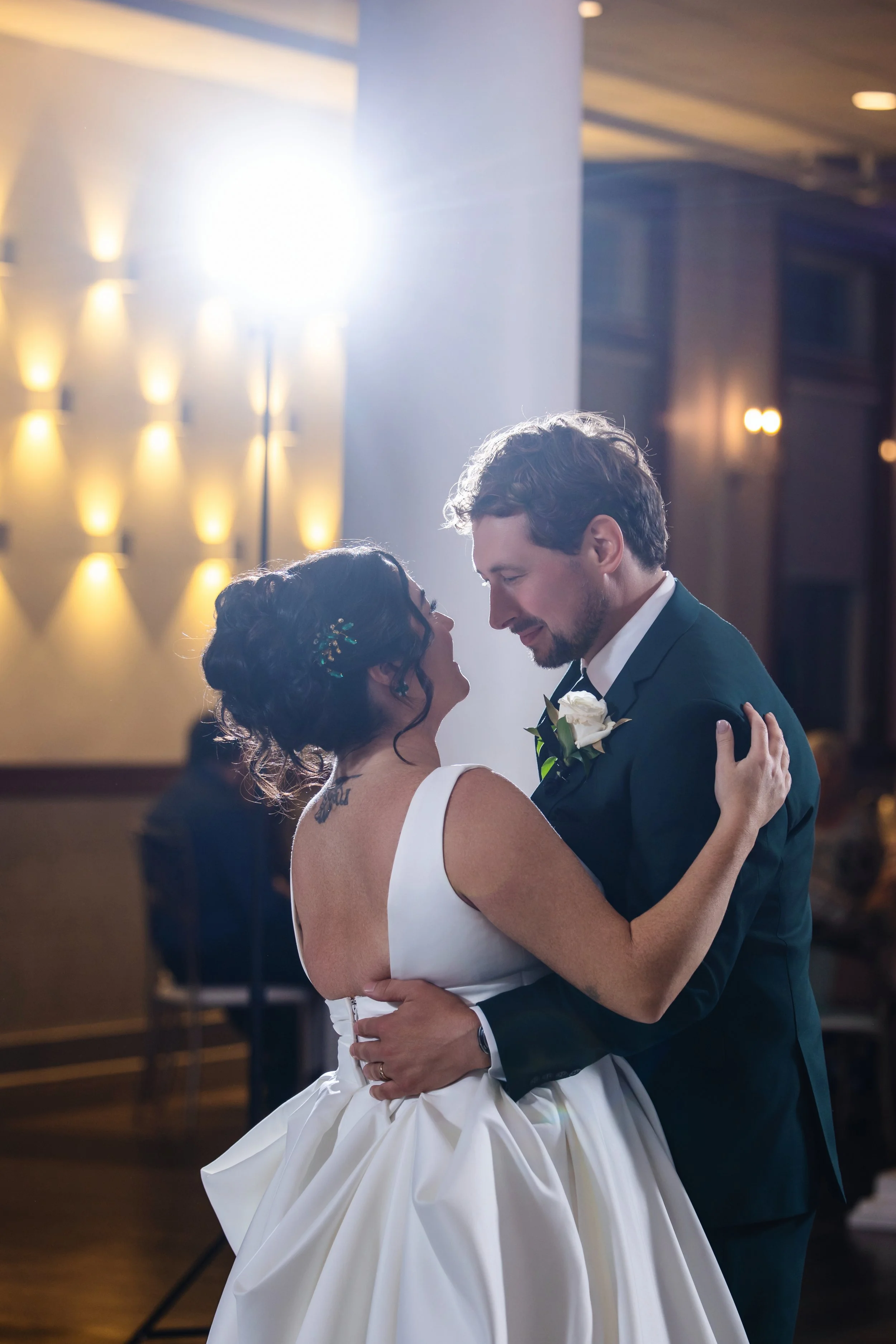 A newlywed couple shares a dance in an elegant venue, with warm lighting and a blurred background.