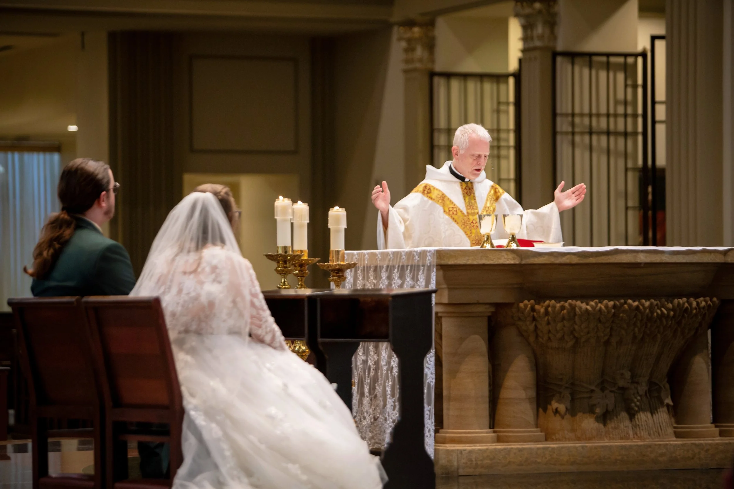 Priest leading a wedding ceremony at the altar with bride and groom seated before him.