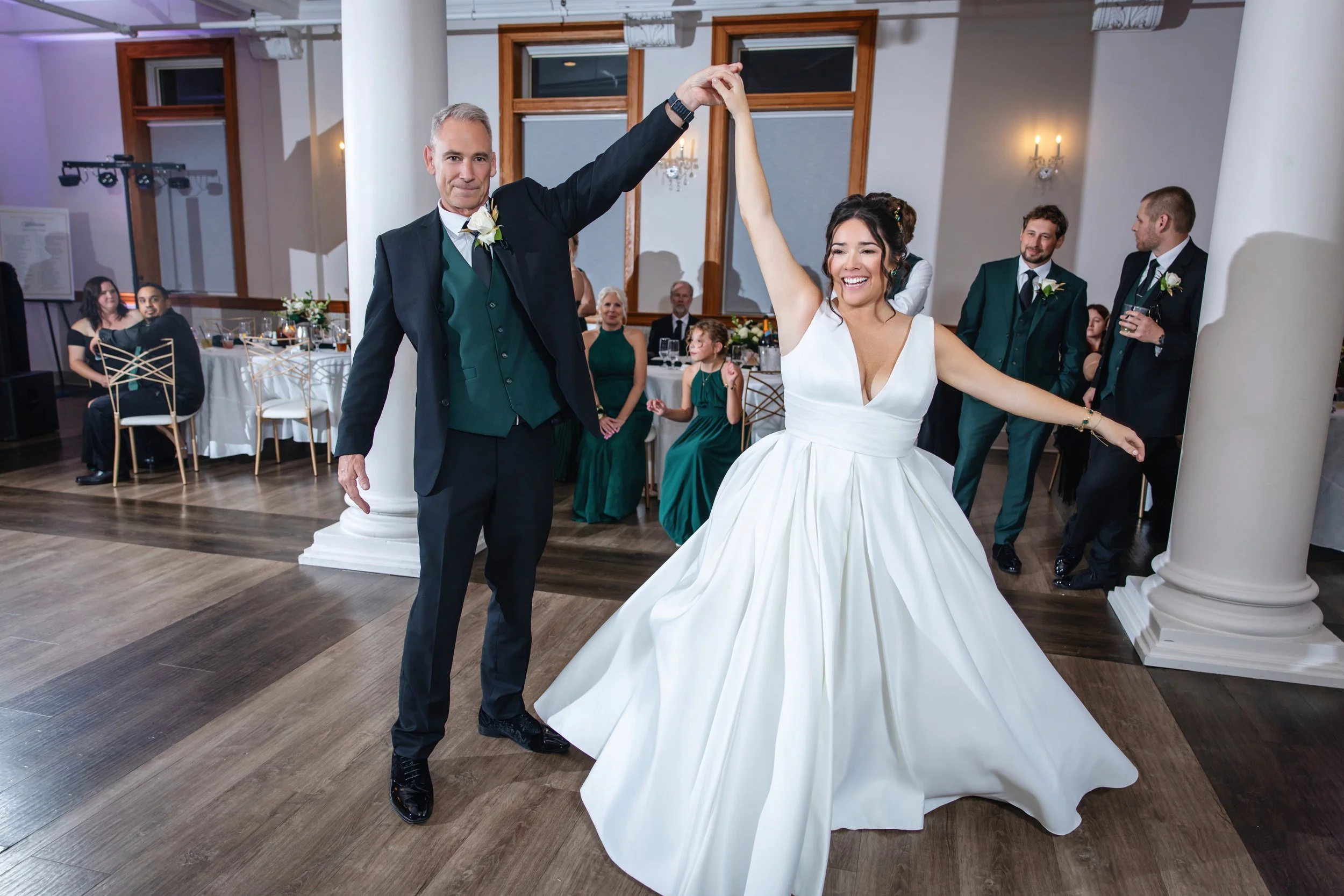 A bride and groom dancing at their wedding reception with guests watching in the background.