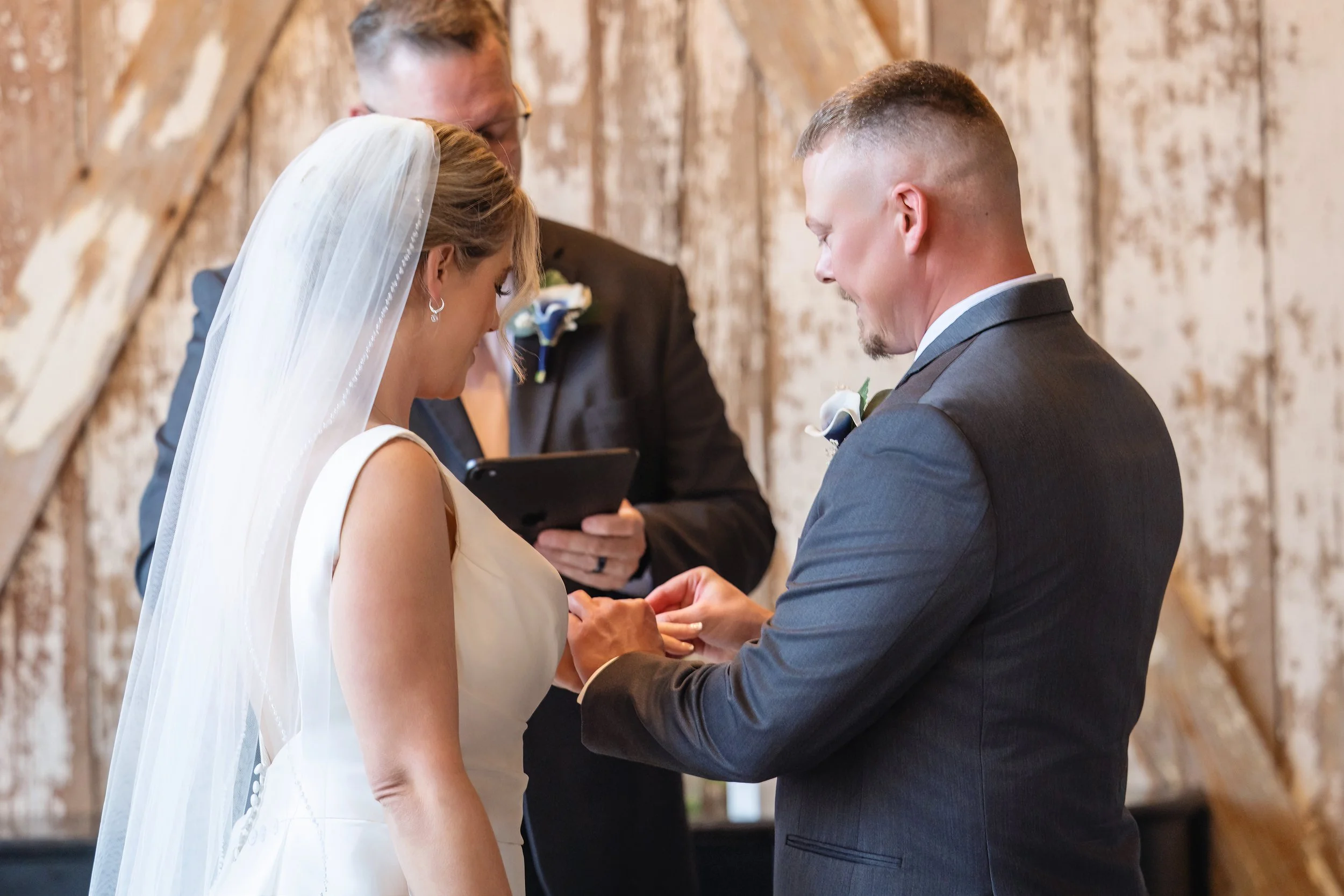 A bride and groom standing face to face during their wedding ceremony, exchanging vows and holding hands with an officiant in the background.