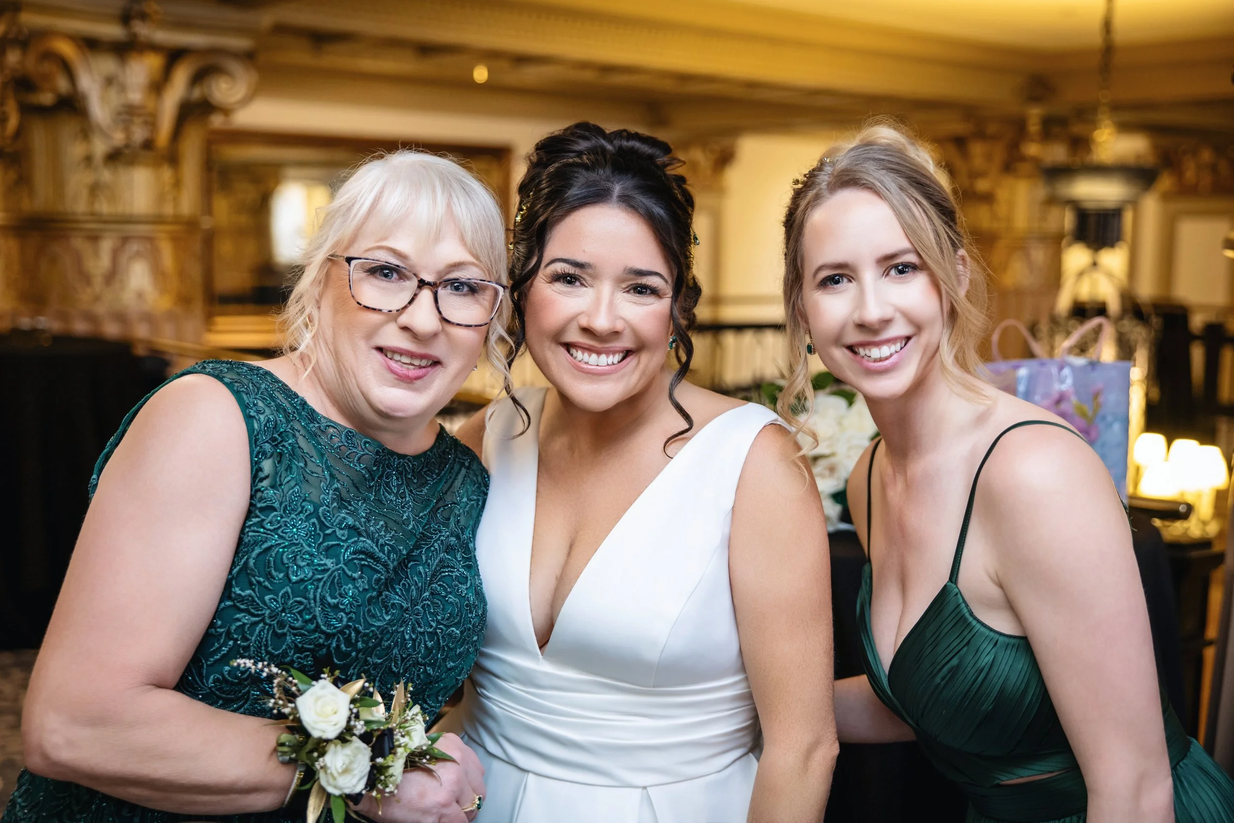 Three women at a formal event posing closely and smiling, with an ornate gold decor background.