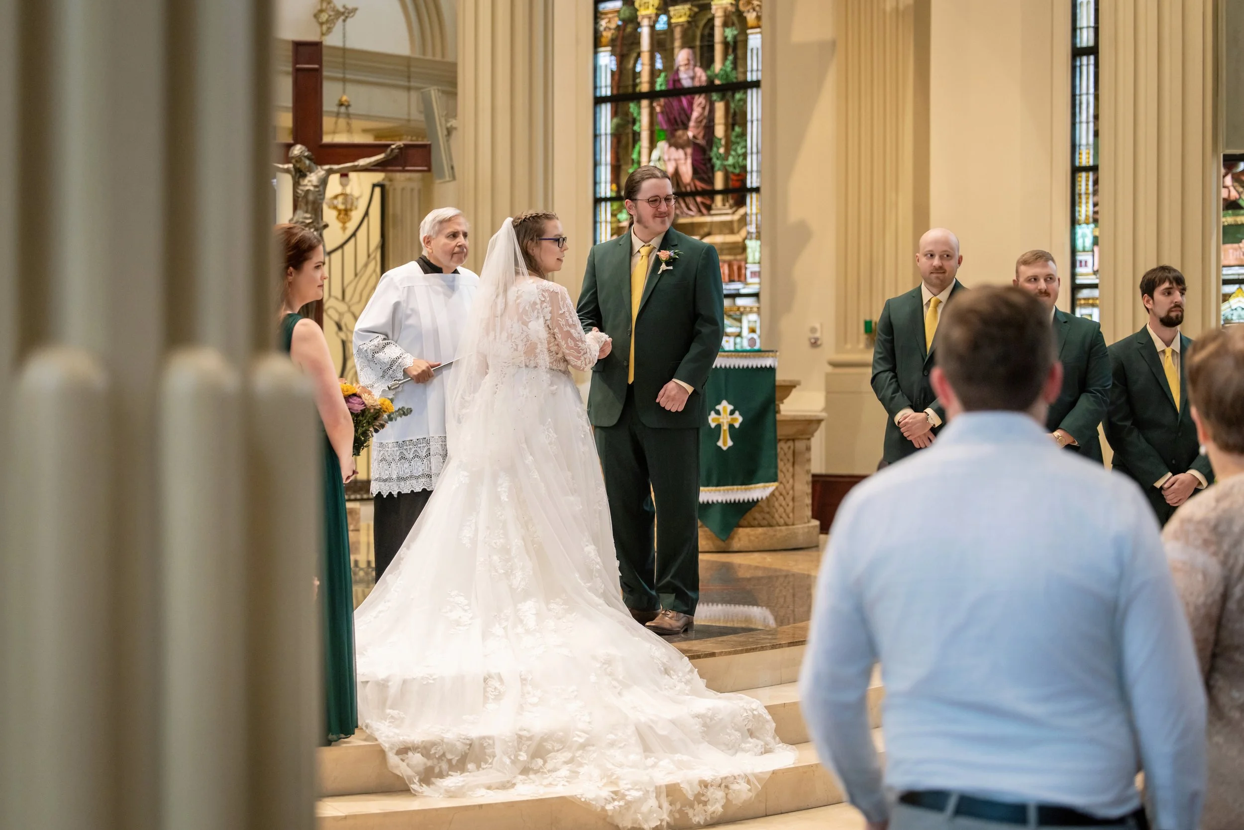A wedding ceremony inside a church showing a bride and groom standing at the altar with several attendants and guests observing.