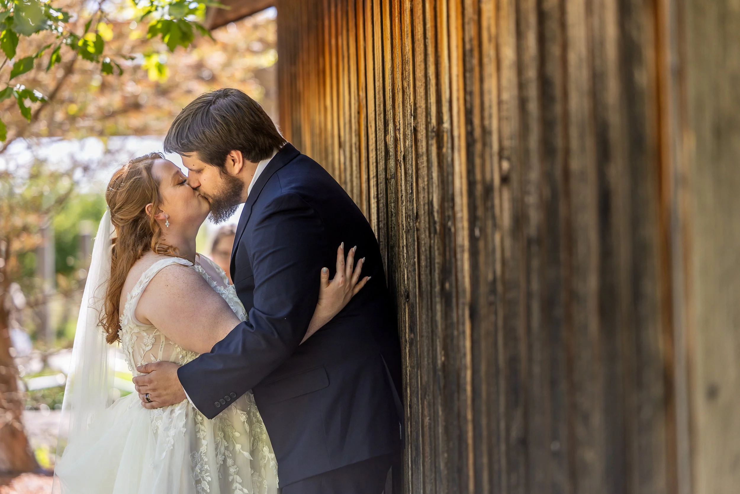 Wedding Photography at Powell Gardens of a bride and groom leaning against a barn.