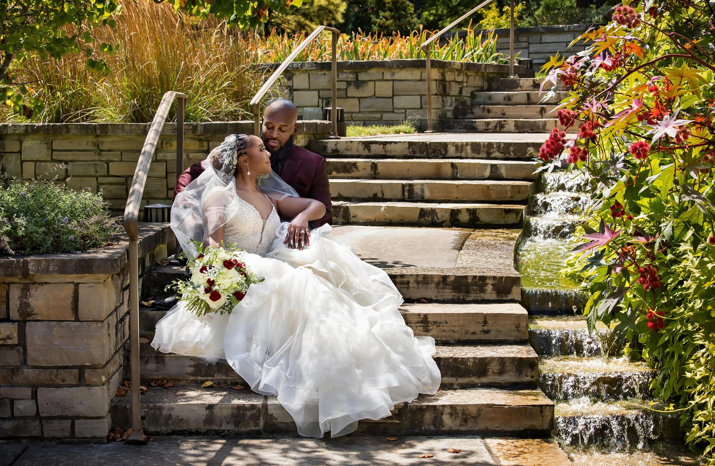 KC Wedding Photography of a Bride and Groom sitting on a step, surrounded by flowers, at the Wedding Venue Powell Gardens