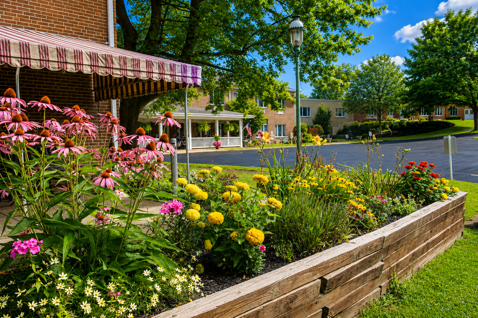 Colorful flower garden in a residential neighborhood with a pink and white striped awning, brick wall, trees, and houses in the background.