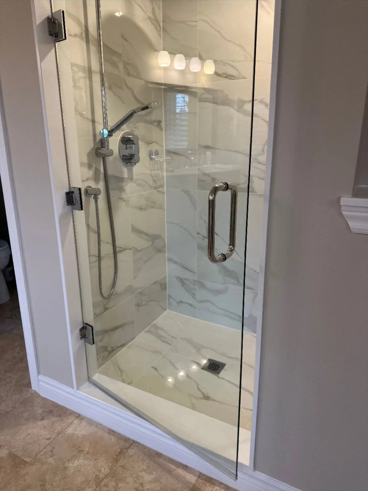 A frameless glass shower door, secured with refined hinges, allows the white tile to shine uninterrupted. The result is a clean, open, and visually calming space, executed with elite precision and timeless appeal #thedaghergroup #homerenovation #bath