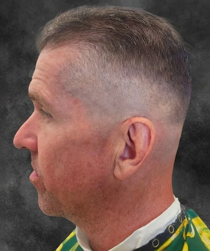 Profile view of a man with a faded hairstyle, wearing a cape typically used in barbershops.