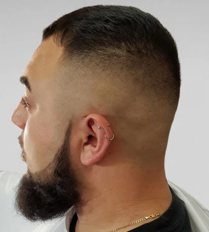 Side profile of a man with a fade haircut, beard, and multiple earrings in his ear.