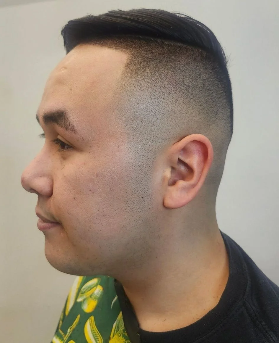 Side profile of a man with a short fade haircut, wearing a colorful shirt with a yellow and green pattern.