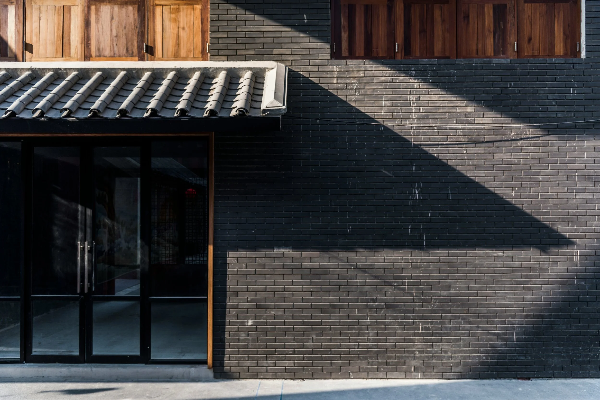Modern building facade with black brick wall and a wooden section with vertical slats, with shadow cast across part of the wall.