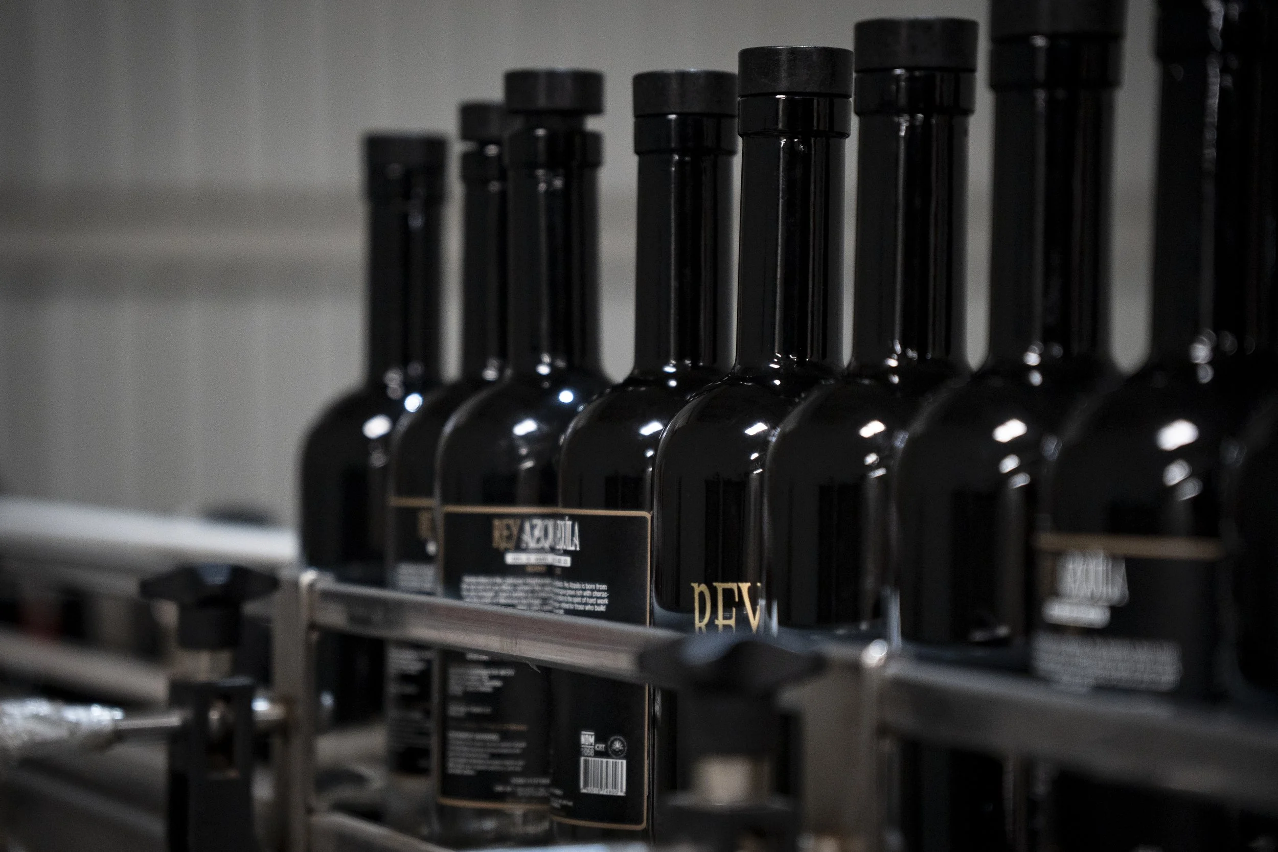 Several black bottles with gold labels on a metal shelf, viewed in a low light setting.