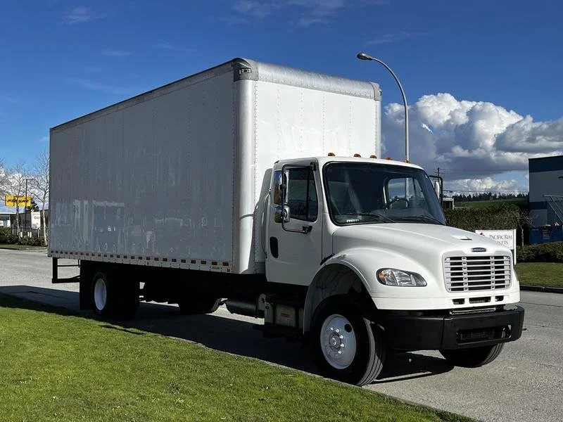 A white box truck parked on the side of the road near a grassy area with a blue sky and clouds in the background.