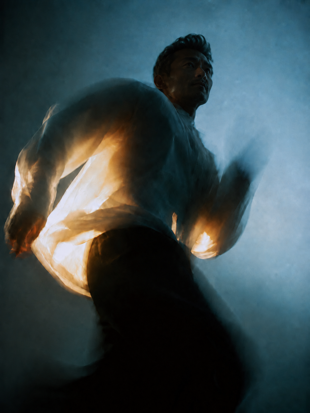 A man running in a dark, smoky environment with a glow from behind, creating a silhouette effect.