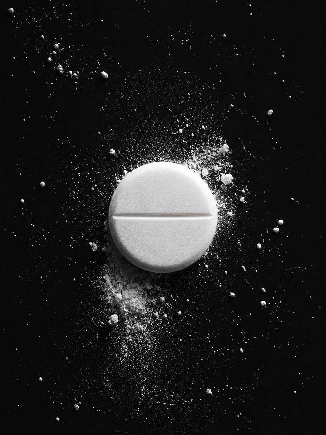 A white pill lying on a black surface with powder scattered around it.
