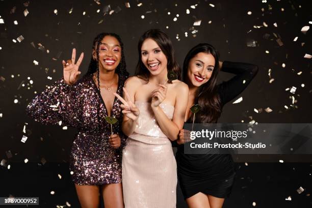 Three young women in party dresses smiling with confetti in the background.